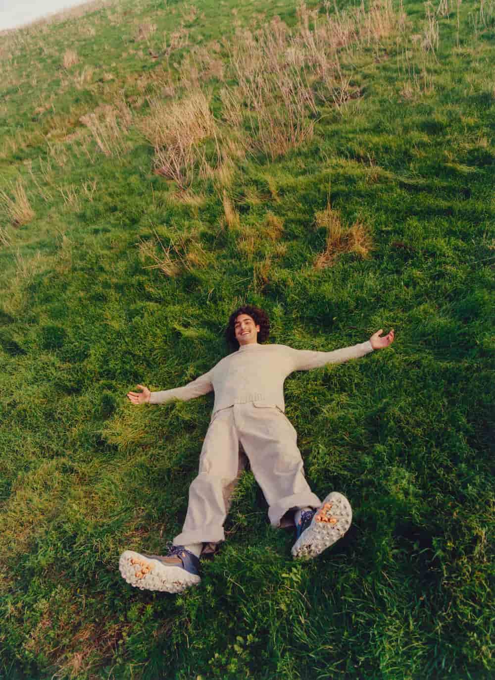 A man lying laughing on the grass with arms and legs waving 