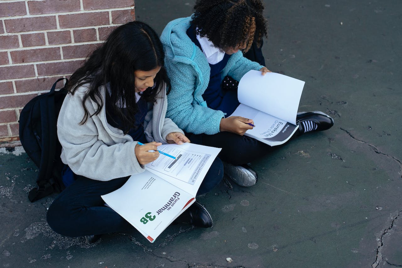 Diverse smart girls solving homework with textbooks together
