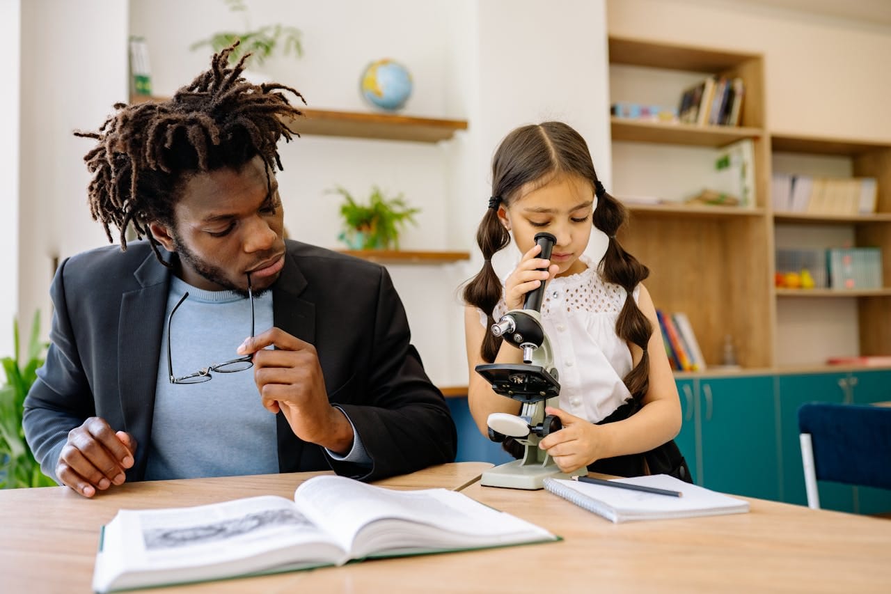 A girl using a microscope beside his teacher