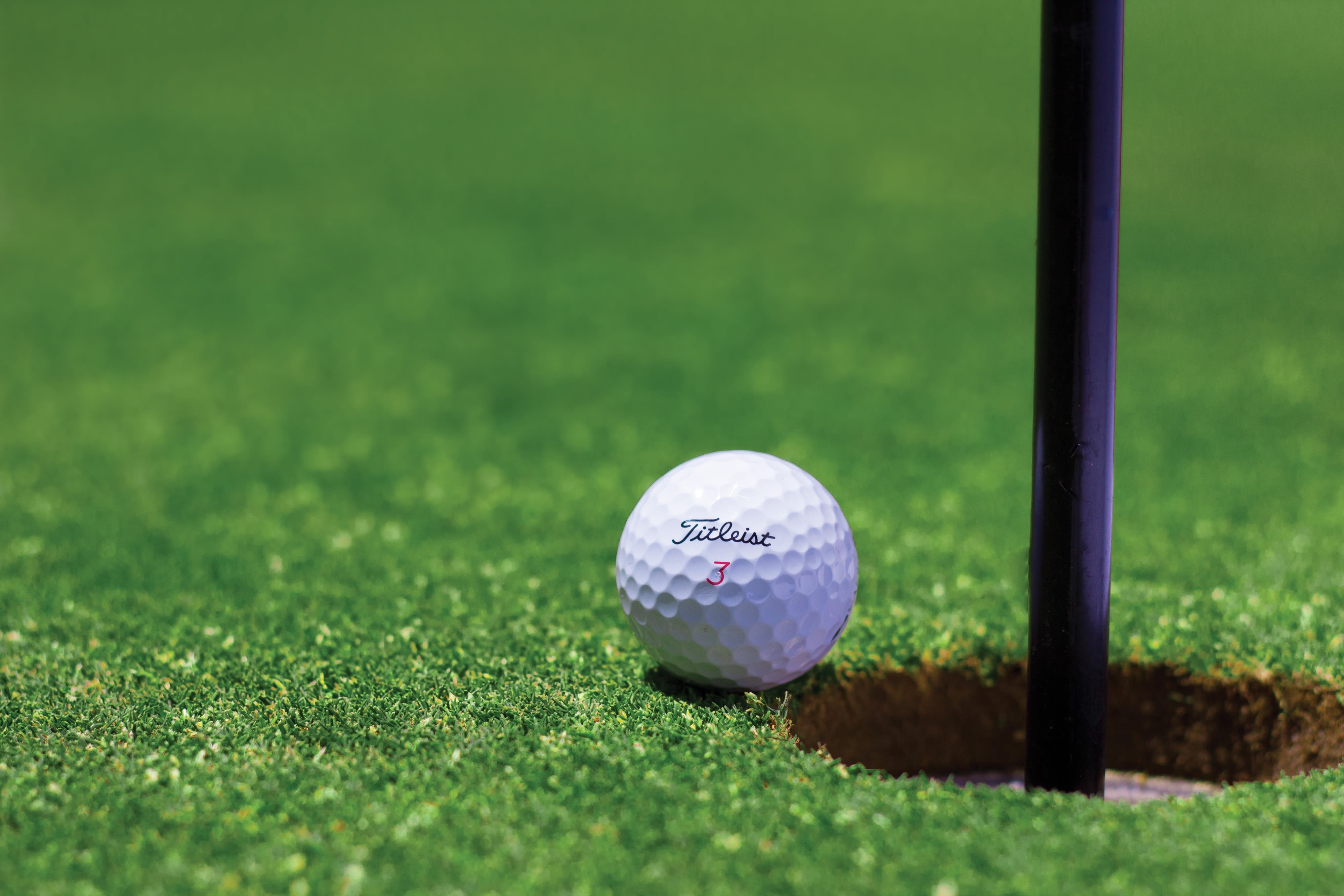 Golf ball next to a hole on the green. 