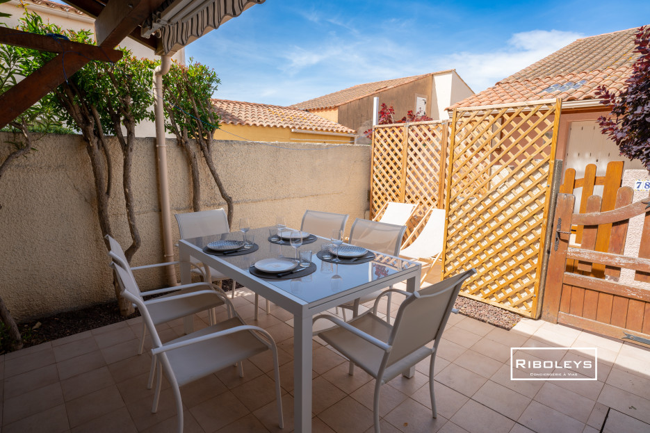 Terrasse intimiste avec espace repas, transats et barbecue charbon