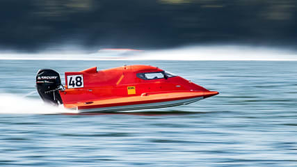 A red speedboat racing across a calm lake, capturing the thrill of outdoor water sports.