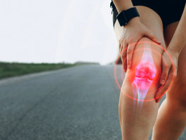 Eine Person hält sich das schmerzende rechte Knie, das von einer digitalen roten Grafik hervorgehoben wird, was auf Gelenkschmerzen oder Arthrose hinweist. Die Person befindet sich auf einer leeren Straße in einer ländlichen Umgebung.