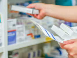 Eine Apothekerin überprüft Medikamente in einem Regal. Sie hält eine Packung in der Hand und prüft die Inhalte, während sie die Medikamente organisiert. Die Regale sind mit verschiedenen Arzneimitteln gut sortiert.