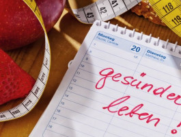 Auf einem Tisch liegen eine Erdbeere, ein Apfel, ein Maßband und ein Kalender mit Aufschrift "gesünder leben".