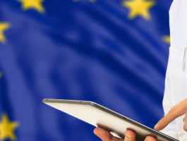 Ein Arzt tippt auf einem Tablet. Im Hintergrund die EU-Flagge.