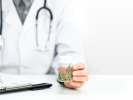 Arzt mit Stethoskop hält ein Glas mit medizinischen Cannabisblüten und schreibt auf einem Klemmbrett eine Verordnung – Symbolbild für Cannabis auf Rezept und ärztlich begleitete Therapie.