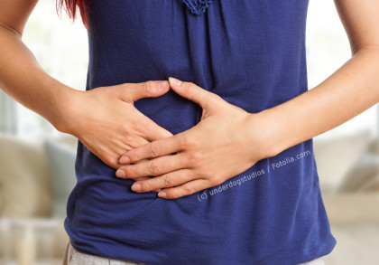 Eine Person in einem blauen Oberteil hält sich ihren Bauch mit beiden Händen, was auf Bauchschmerzen oder Unwohlsein hindeutet.