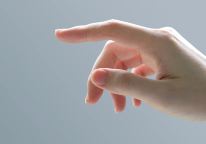 Eine Nahaufnahme einer Hand mit ausgestrecktem Zeigefinger vor einem grauen Hintergrund.