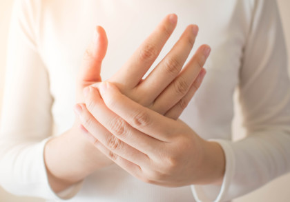Nahaufnahme einer Person, die ihre schmerzende Hand hält und eine weiße Kleidung trägt.