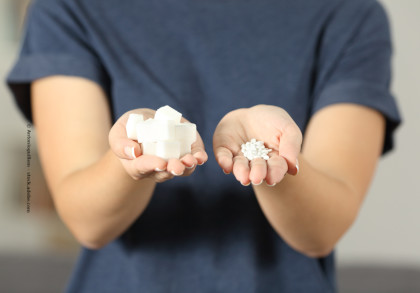 Eine Person in einem dunkelblauen T-Shirt hält in einer Hand mehrere weiße Zuckerstücke und in der anderen Hand weiße, kleine Tabletten.