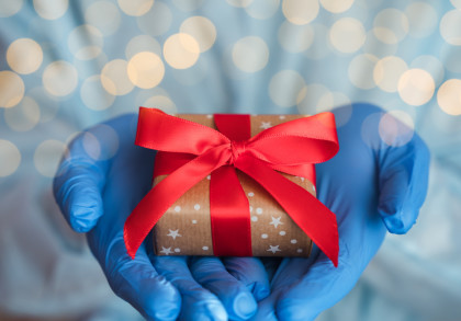 Hände in blauen Handschuhen halten ein kleines Geschenk mit großer roter Schleife
