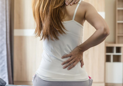 Eine Frau, die sich an den Rücken greift und Schmerzen hat.