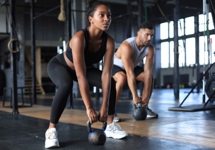 Frau und Mann trainieren in Fitnessstudio mit Kugelhanteln