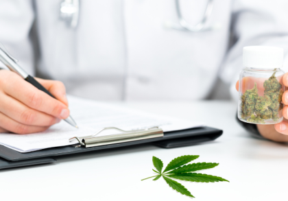 Arzt mit Stethoskop schreibt Rezept und hält Dose mit medizinischem Cannabis. Auf dem Tisch liegt ein Cannabisblatt – Symbolbild für Cannabis auf Rezept.