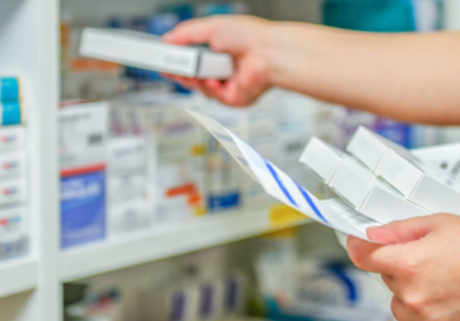 Eine Apothekerin überprüft Medikamente in einem Regal. Sie hält eine Packung in der Hand und prüft die Inhalte, während sie die Medikamente organisiert. Die Regale sind mit verschiedenen Arzneimitteln gut sortiert.