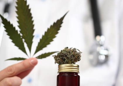 Arzt mit Stethoskop hält Cannabisblatt neben Glasflasche mit Cannabisblüte – Symbolbild für medizinisches Cannabis und ärztliche Verschreibung in Deutschland.