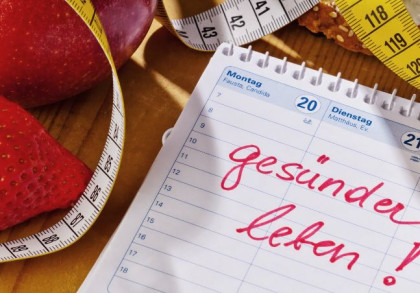 Auf einem Tisch liegen eine Erdbeere, ein Apfel, ein Maßband und ein Kalender mit Aufschrift "gesünder leben".