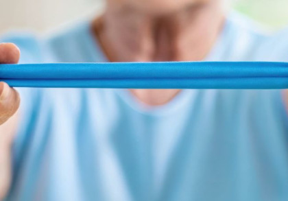 Eine ältere Person spannt ein Theraband zwischen den Händen.