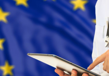 Ein Arzt tippt auf einem Tablet. Im Hintergrund die EU-Flagge.