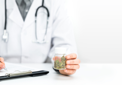 Arzt mit Stethoskop hält ein Glas mit medizinischen Cannabisblüten und schreibt auf einem Klemmbrett eine Verordnung – Symbolbild für Cannabis auf Rezept und ärztlich begleitete Therapie.
