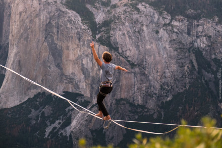 Eine Person balanciert auf einem Hochseil vor einer spektakulären Berglandschaft. Die Felswände im Hintergrund sind beeindruckend und steil.