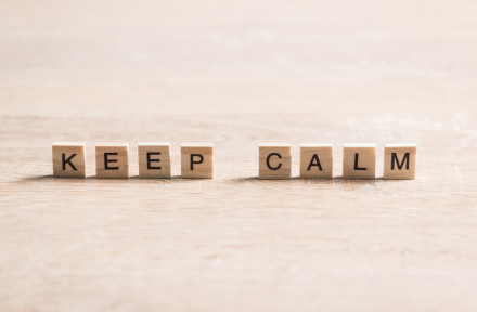 Holzwürfel auf einem Holztisch, die das englische Wort "KEEP CALM" buchstabieren.