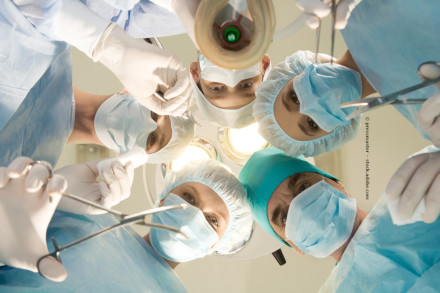 Das Bild zeigt eine Gruppe von Chirurgen in einem Operationssaal, die nach unten in die Kamera schauen. Sie tragen alle Operationskleidung inklusive Masken, Hauben und Handschuhen.