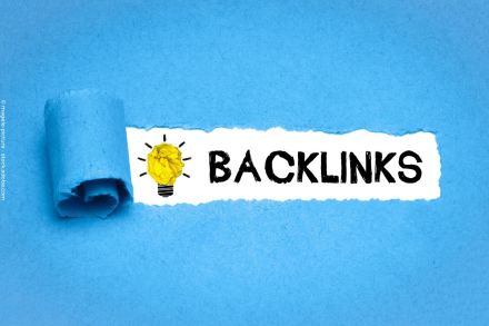 Zu sehen ist ein blaues Papier, das teilweise aufgerollt ist und den darunter liegenden weißen Hintergrund mit dem Wort "BACKLINKS" und einer symbolischen Glühbirne hervorbringt. Die Glühbirne besteht aus zerknittertem gelben Papier und strahlt Ideen aus.