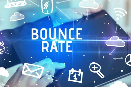 Ein Tablet wird von zwei Händen bedient. Der Text "Bounce Rate" steht in der Mitte, umgeben von Symbolen wie einer Wolke, einem Handy, einem Wecker, einem Umschlag und einer Lupe. Diese Symbole repräsentieren verschiedene digitale Elemente und Funktionen.