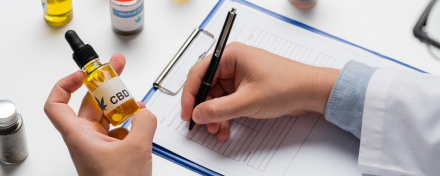 Arzt oder Ärztin hält eine CBD-Öl-Flasche in der Hand und füllt ein Rezeptformular aus – Symbolbild für die ärztliche Verschreibung von medizinischem Cannabidiol.