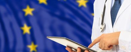 Ein Arzt tippt auf einem Tablet. Im Hintergrund die EU-Flagge.
