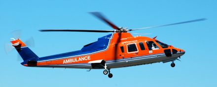 Orange-blauer Rettungshubschrauber (Air Ambulance) im Flug vor blauem Himmel, medizinischer Notfalleinsatz und schneller Patiententransport durch ein spezialisiertes Notfallteam.
