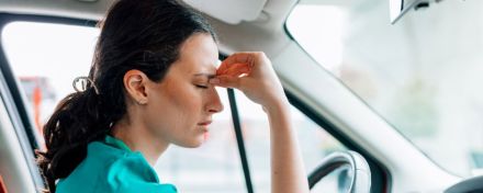 Eine Ärztin fasst sich erschöpft an die Stirn. Sie sitzt im Auto und hat Kopfschmerzen.