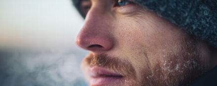 Nahaufnahme eines Mannes mit Mütze im Winter: gerötete Nase, kalte Gesichtshaut und sichtbarer Atem in frostiger Luft.