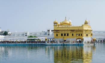 a large yellow boat in the water with Harmandir Sahib in the background