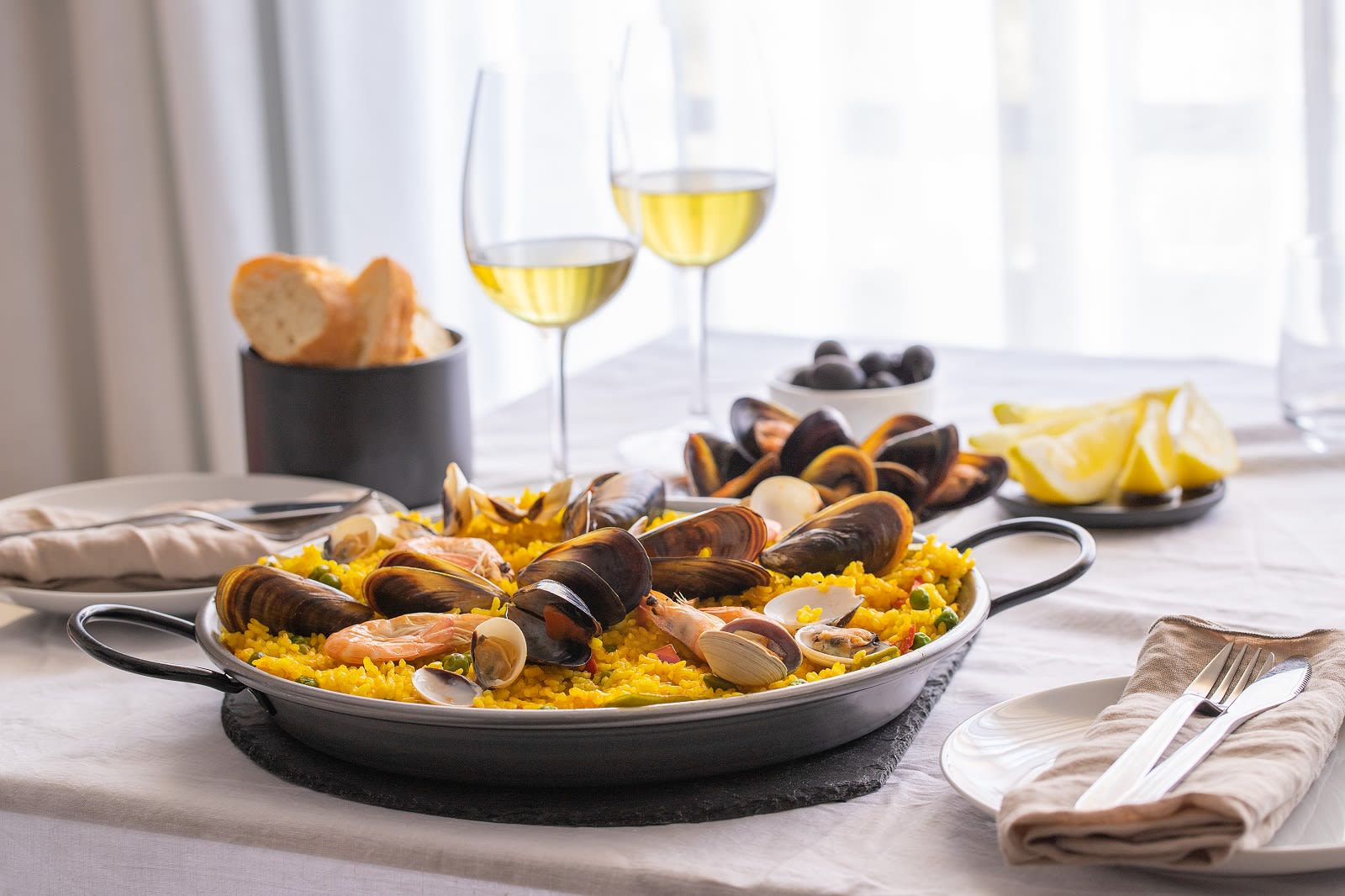 Seafood Paella with prawns, clams, mussels on saffron rice and vegetables and bottle of white wine on restaurant table Food in spain