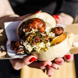 Argentina street food, traditional choripan sandwich with chorizo sausage, tomato, goat cheese, and chimichurri sauce at a street food market