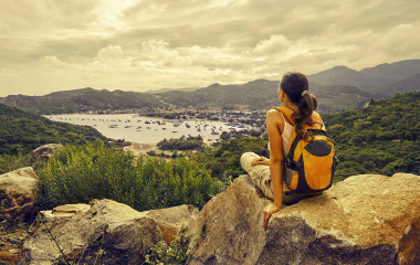 Woman traveler looks at the edge of the cliff on the sea bay of mountains in the background