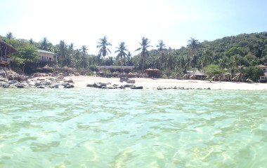 Blick vom kristallklaren Wasser zum Sandstrand mit Palmen und Lodge auf Ko Tao, Thailand