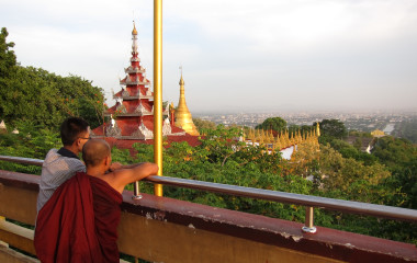 Ein junger Mönch und ein Junge in Myanmar genießen die Aussicht vom Mandalay Berg auf die Stadt und die goldene Pagode im Hintergrund