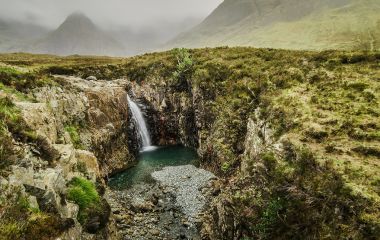 Enchanting Travels UK & Ireland Tours Waterfall in a cloudy day at the Fairy Pool trail, Isle of Skye, Scotland, UK