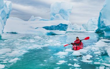 Mann fährt im Kajak durch die Eisberge der Antarktis