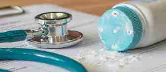 Close-up of a stethoscope and a spilled bottle of baby powder on a medical document. The baby powder is shown scattering over the paper, next to the teal-colored stethoscope, indicating a medical or healthcare setting.