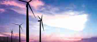 Silhouettes of wind turbines stand against a vibrant sky painted with shades of blue, purple, and pink during sunset. The turbines are aligned, with the largest in the foreground and smaller ones receding into the distance.