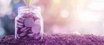 A small plant with green leaves emerges from a glass jar filled with coins, placed on a mound of soil. The background is softly lit with a bokeh effect, creating a warm and radiant atmosphere, symbolizing growth and investment.