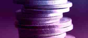 A stack of coins precariously balanced, viewed up close and illuminated with dramatic blue and purple lighting, creating a vivid contrast and giving the coins a metallic sheen. The background is blurred, keeping the focus on the coins.