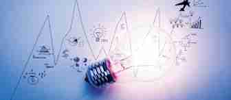 A glowing light bulb lies on a paper with various hand-drawn business-related icons, including graphs, a money bag, gears, and a plane. The background shows a blue-tinted zigzagging line graph, leading to the text "100%" at the top right corner.
