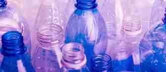 A collection of empty, open plastic bottles in varying shades of blue, purple, and clear. The bottles are arranged closely together, creating a dense and colorful pattern. The image highlights the texture and reflective surfaces of the bottles.