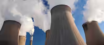 A series of large, industrial cooling towers emitting steam against a clear, blue sky. The towers are cylindrical and widen at the top, with white steam billowing out, indicating active operation, typical of power plants or factories.